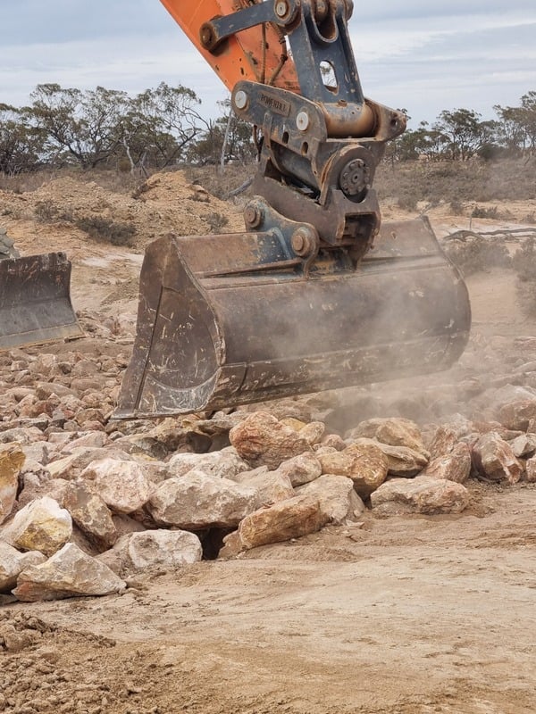 An excavator is engaged in digging operations, positioning rocks on the ground at a construction location.
